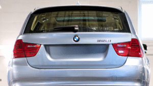 Rear view of a silver BMW 528i station wagon with red tail lights, a rear wiper, and water droplets on the rear window.