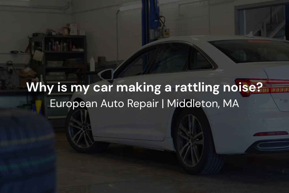 A white car, reported to be making a rattling noise, is parked inside an auto repair shop garage with equipment and shelves visible in the background.