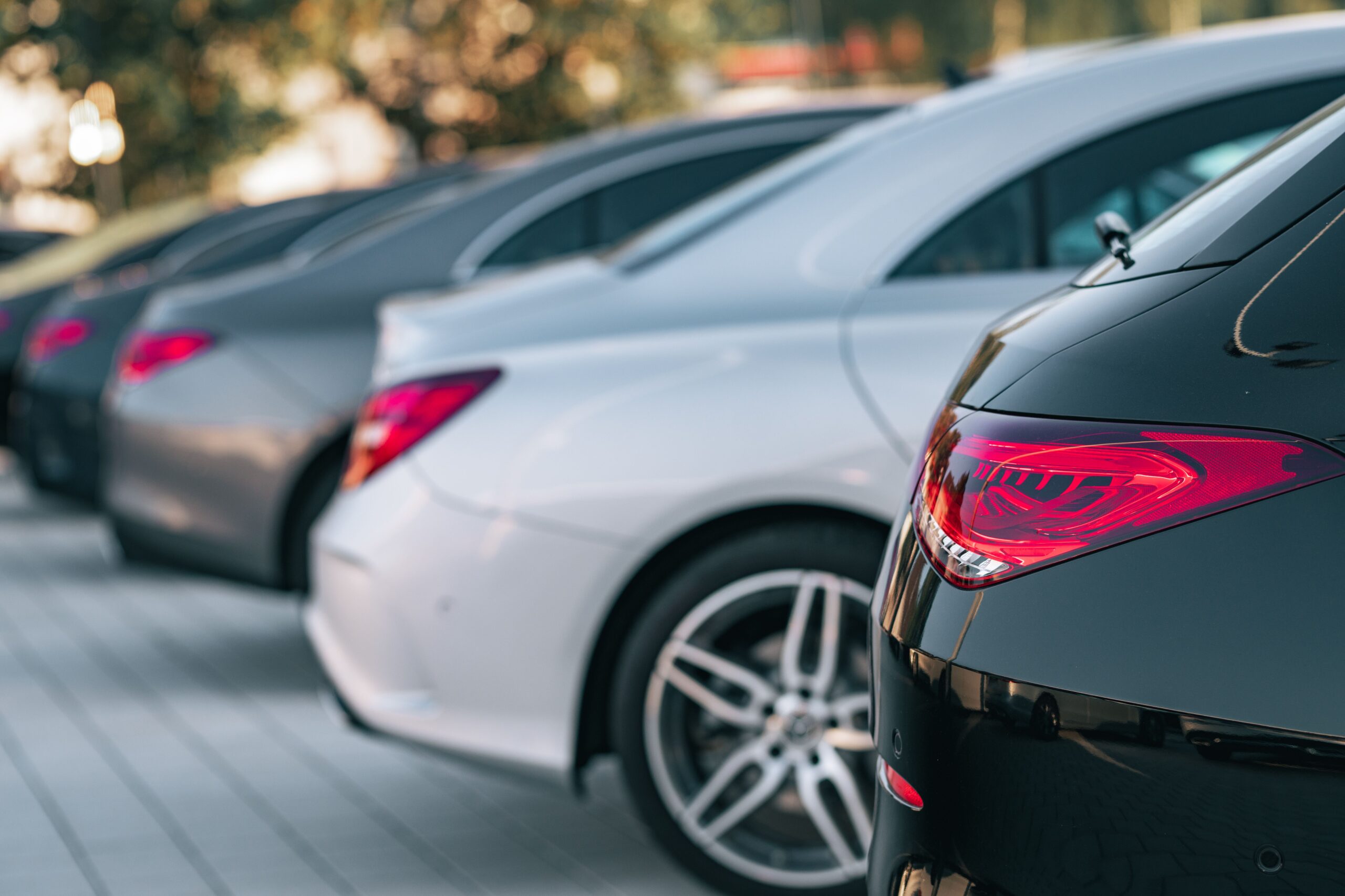 A row of parked modern sedans in various colors, seen from the rear in an outdoor parking lot.